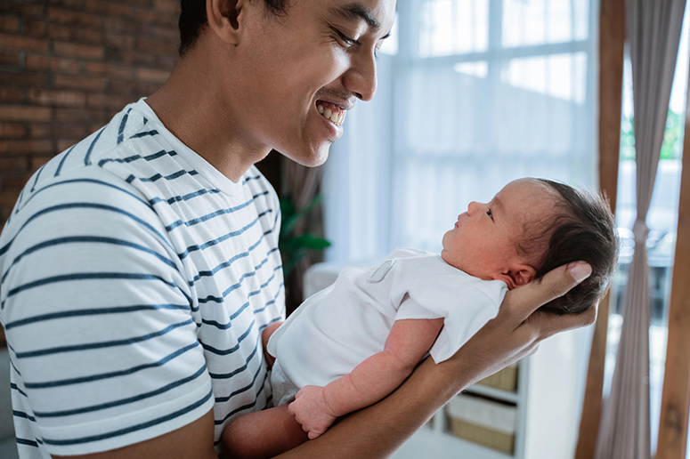 dad smiling and holding newborn on his arm